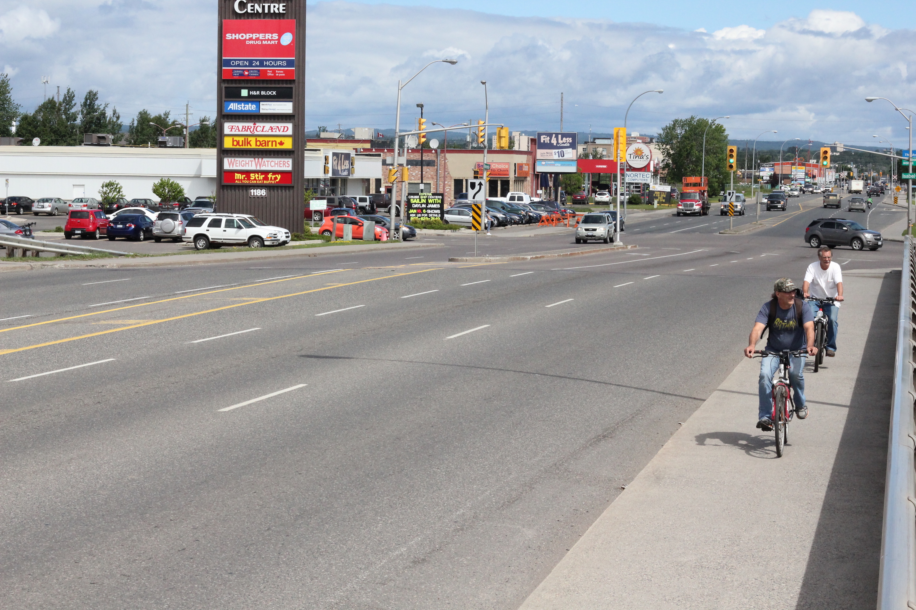 Two men ride bikes in normal clothing on the sidewalk of Memorial Avenue near Intercity